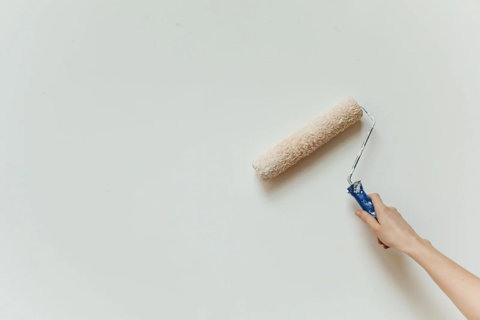 Rouleau chargé de peinture blanche déposant une passe sur une surface lisse